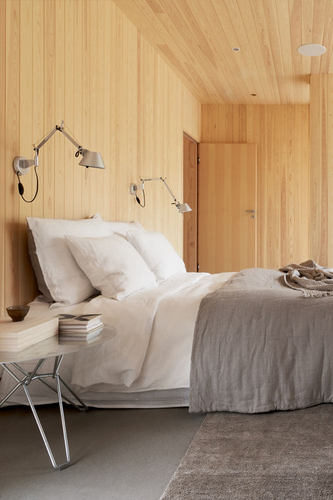 Roots Living pellavalakanoilla pedattu sänky makuuhuoneessa, jossa on paneloidut seinät ja betonilattia