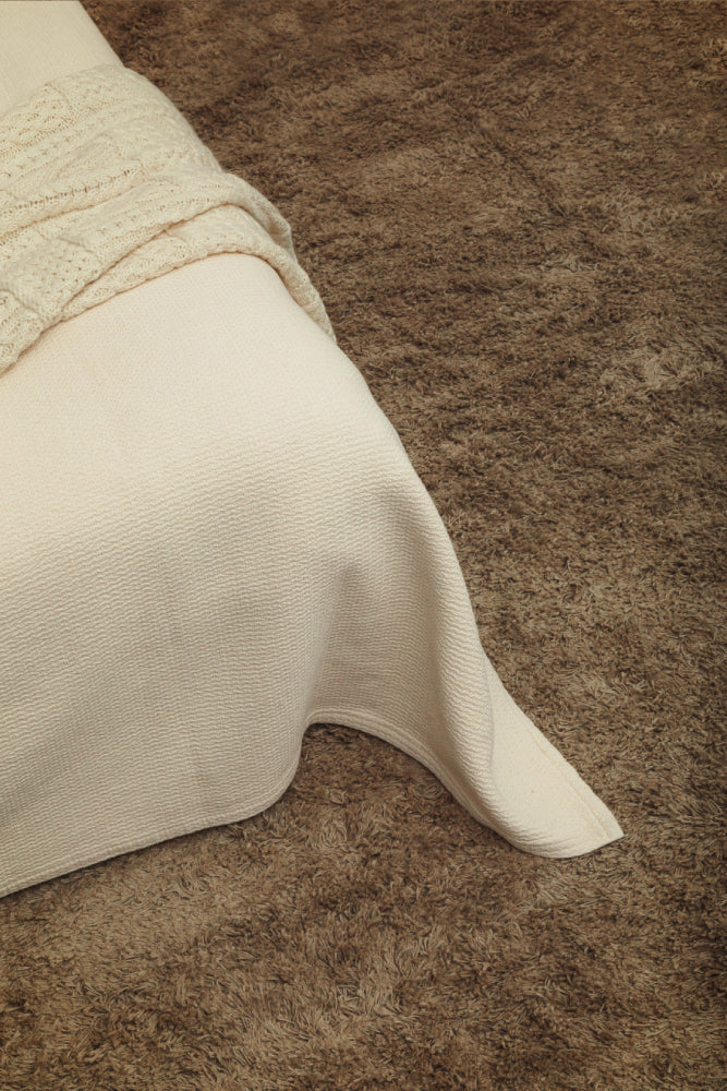 Luonnonvalkoisen Polku-päiväpeiton kulma kuvattuna luonnonväristä pellavamattoa vasten.