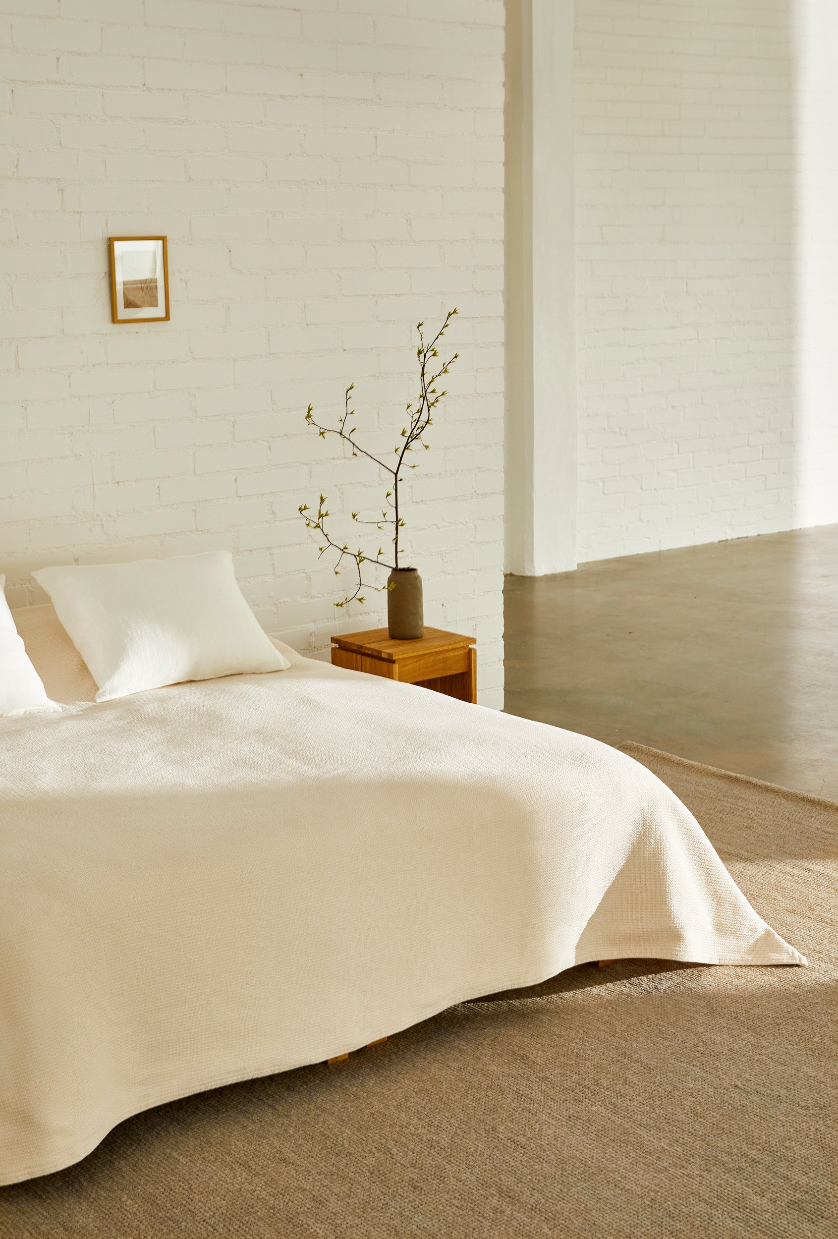 Vaalea sävyinen makuuhuoneen sisustus, jossa sänky on pedattu luonnonvalkoisella päiväpeitolla. Roots Livingin Polku-päiväpeitto on Ulla Koskisen suunnittelema.