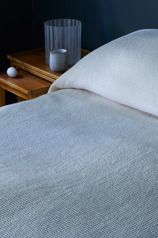 Luonnonvalkoisen Polku päiväpeiton tekstuuri kuvattuna läheltä tummansinisessä makuuhuoneessa.