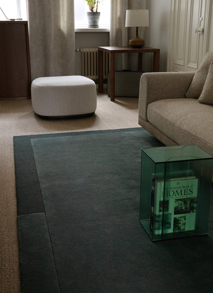 Sininen Geo One -villamatto, jonka päällä on lasinen sohvapöytä ja vaalea kangassohva. Taustalla valkoinen rahi ja pähkinän sävyinen pöytä.