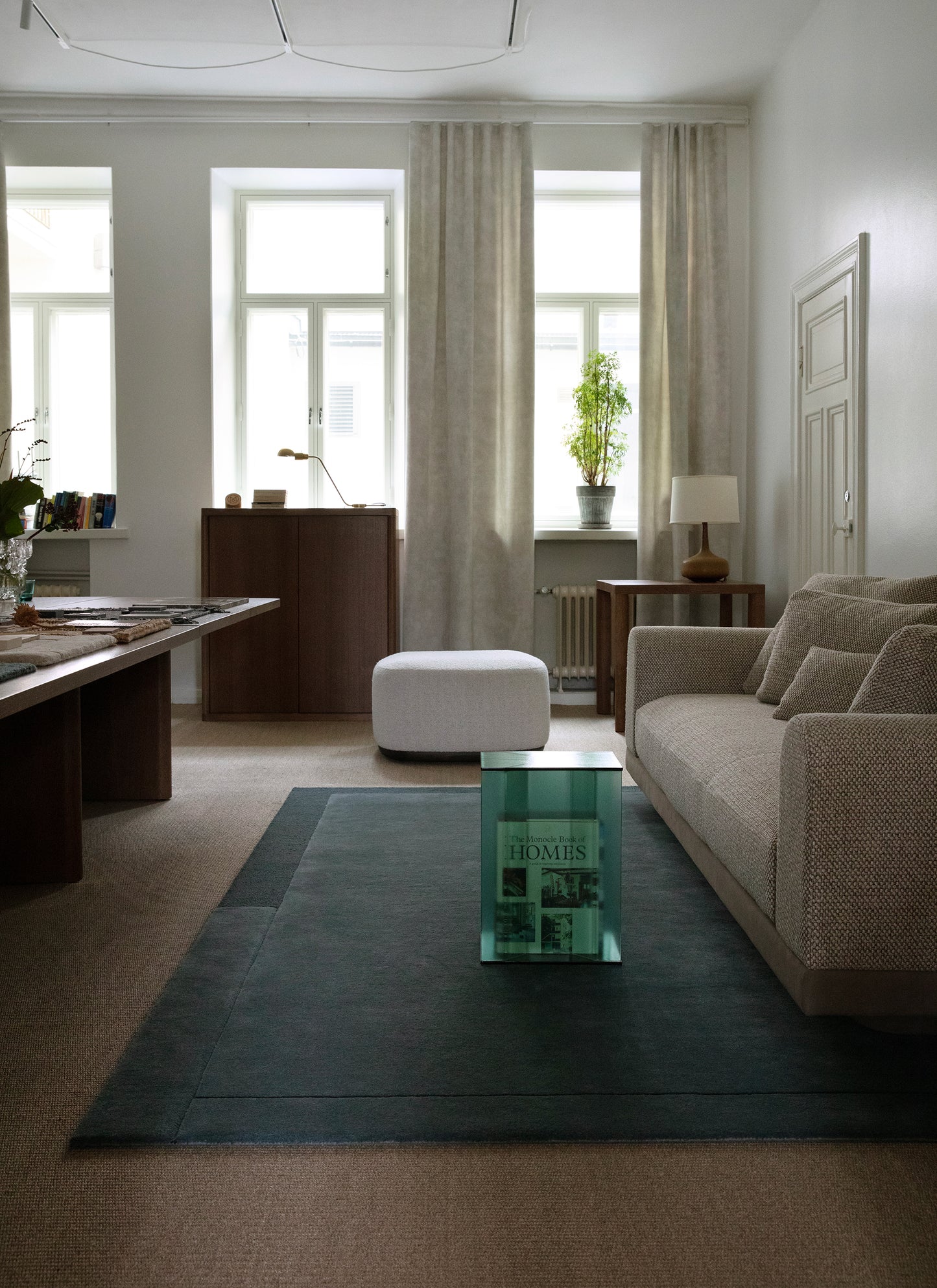 Sininen Geo One -villamatto lattialla vaalean sohvan edessä. Maton päällä lasinen sohvapöytä. Taustalla korkeat ikkunat ja verhot.