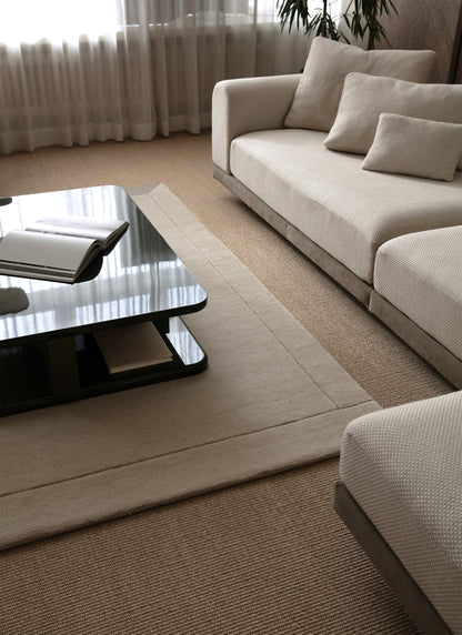 Vaalea sohva ja vaalea Geo One -villamatto valoisassa tilassa. Sohvapöydällä avoin kirja. 