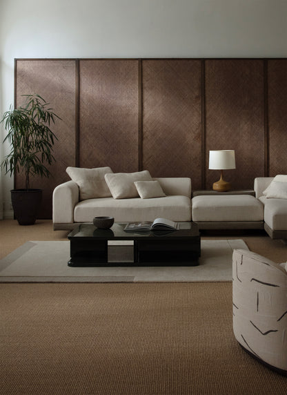 Matalan vaalean sohvan edessä kiiltävä sohvapöytä, jonka alla vaalea Geo One -villamatto. Taustaseinä tummanpähkinän sävyistä paneelia. Kulmassa viherkasvi. 