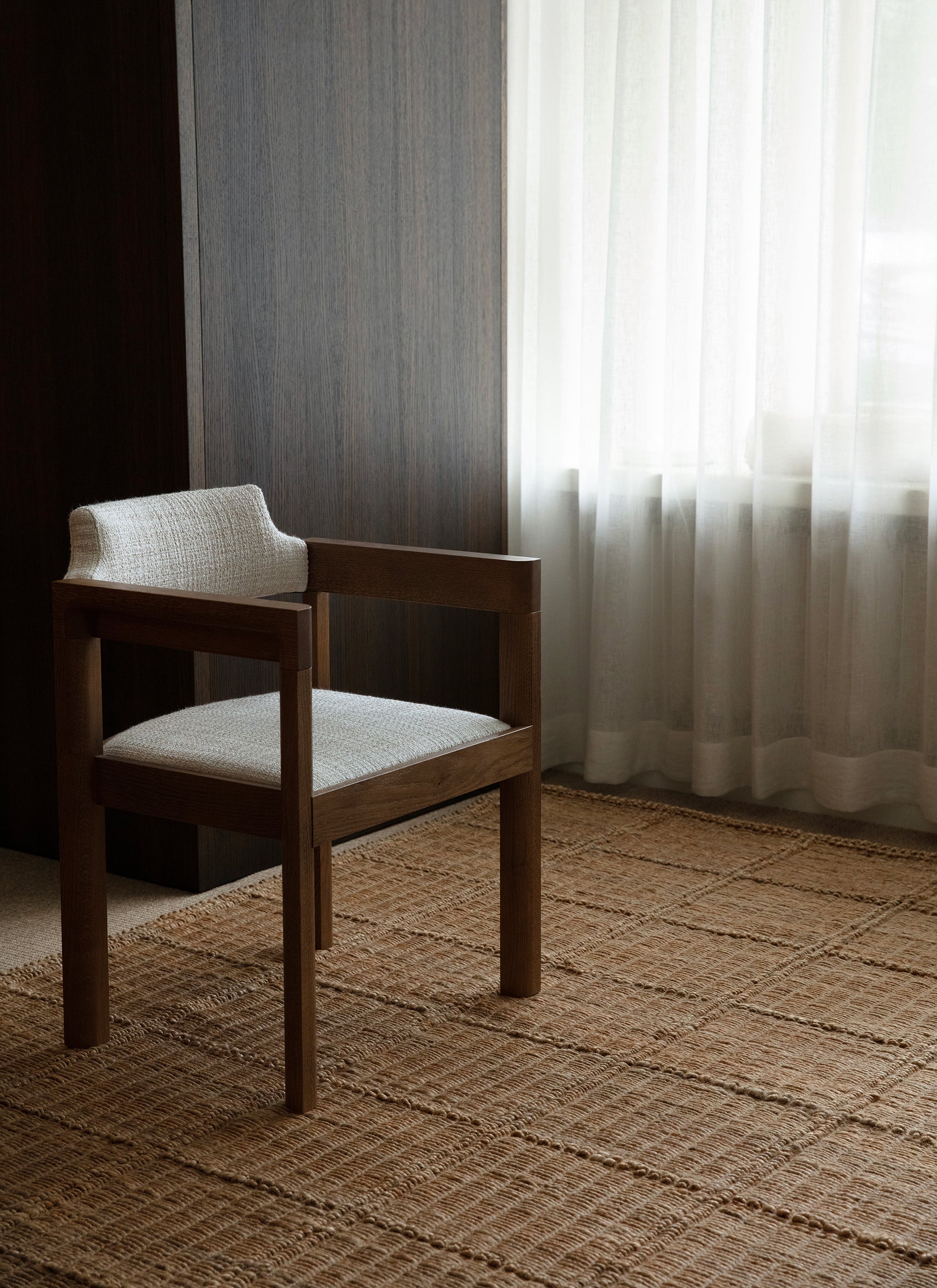 Tuoli käsinojilla Waffle Square -hamppumaton päällä. Vaaleiden verhojen läpi siivilöityy valoa.