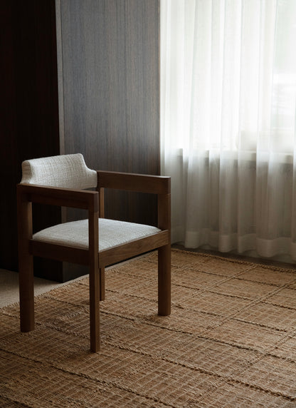 Tuoli käsinojilla Waffle Square -hamppumaton päällä. Vaaleiden verhojen läpi siivilöityy valoa.